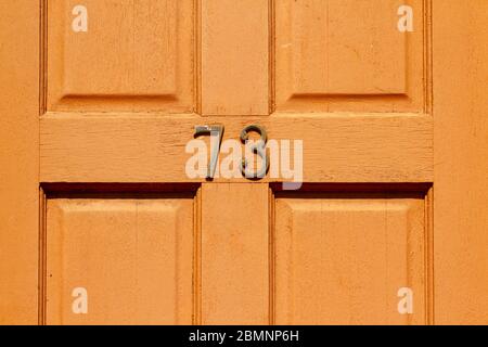 House number 73 on a light wooden front door Stock Photo