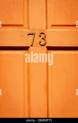 House number 73 on a light wooden front door Stock Photo