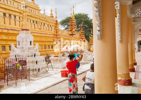 Bagan Myanmar - October 29 2013; ornate architectural facades of Buddhist Shwezigon Pagoda and monastery. with woman vendor carrying goods for sale on Stock Photo