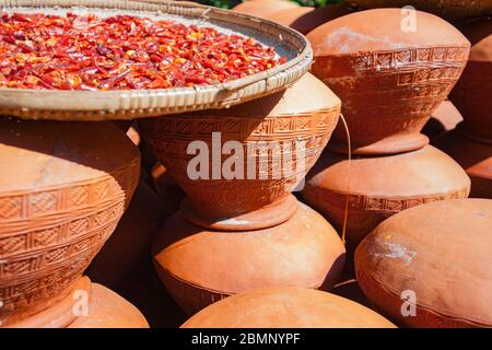 Rows of completed terracotta pots of urns being manufactured in remote Burmese village with tray chillies drying on top. Stock Photo