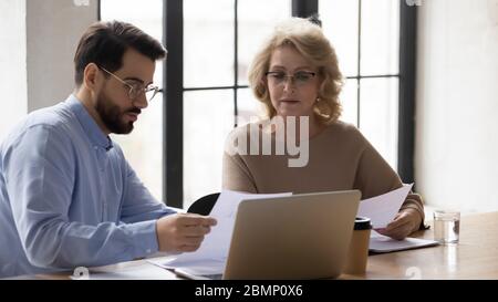 Diverse serious businessman and mature businesswoman reading finance report. Stock Photo