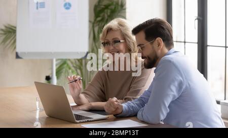 Mature businesswoman using laptop with young businessman looking at screen. Stock Photo