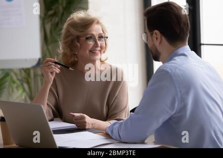 Smiling mature 60 year old businesswoman listening businessman. Stock Photo