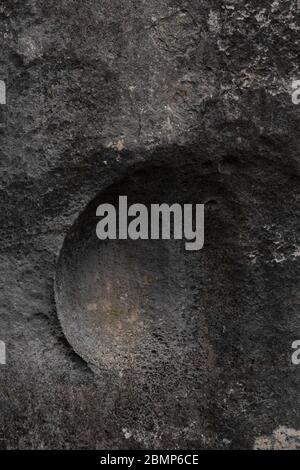 Abstract background of rough textured dark rock surface with large concave carving to centre Stock Photo