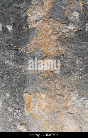 Abstract background of rough textured dark rock surface with brown orange mottled pattern to centre Stock Photo
