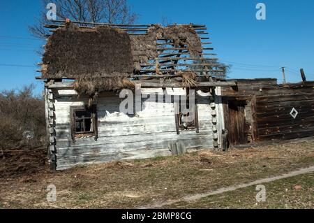 Old dilapidated wooden house with whitewashed walls and thatched leaky roof against the sky. Behind the house you can see a modern electric pole and w Stock Photo