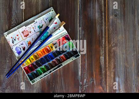 Set of watercolor paints and paintbrushes for painting closeup on wooden table. Copy space flat lay Stock Photo
