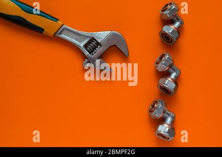 Creative orange background with hand tools and plumbing fittings. Adjustable wrench and three bronze corner fittings for multilayer water pipes. View Stock Photo