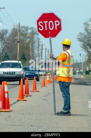 Road worker holds stop sign to direct traffic while a crew repairs a road Stock Photo