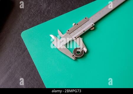 Ball bearing and vernier caliper on a black and turquoise background. Metal vernier caliper with decimal measurement system. Calculation of the dimens Stock Photo