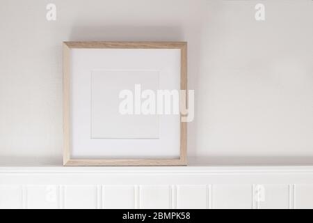 Closeup of square empty wooden picture frame on shelf. White beadboard wainscot wall paneling background. Scandinavian interior, home design. Art conc Stock Photo