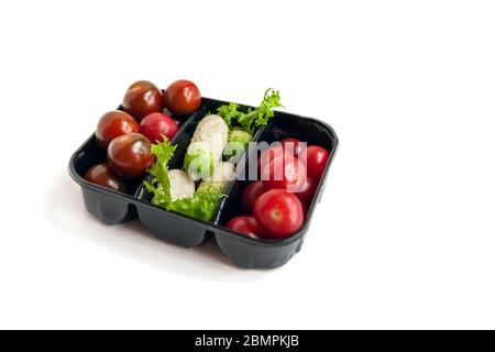 Fresh ripe little cocktail cucumbers and cherry tomatoes in a plastic black container. Isolated on white, copy space. Stock Photo