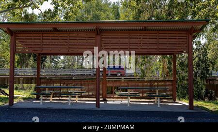 A picnic shade structure beside a bridge overpass with a red car traveling on the highway Stock Photo