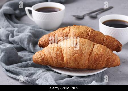 Two fresh croissants and two cups of coffee on a light grey concrete background. Breakfast or lunch concept. Horizontal format Stock Photo