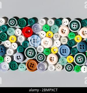 Colorful mixed sewing buttons on grey background, flat lay. Items for sewing clothes.  Top view, square cropping. Stock Photo