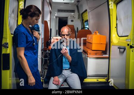 Ambulance car, a young nurse is giving an oxygen mask to an injured man in a blanket Stock Photo