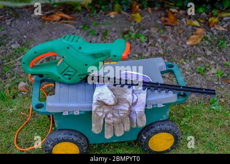 47 Electric hedge trimmers and gardening gloves on a plastic tool box in an English country garden Stock Photo