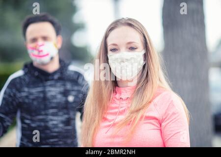 A young couple walking in the neighborhood wearing fabric face masks. Covering face in public is recommended by CDC in many countries during to Covid Stock Photo