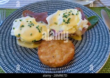 Eggs Benedict with Hollandaise and hash browns served on a plate outside Stock Photo