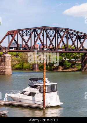 A pleasure boat moored to a dock on the Allegheny River with a railroad bridge behind it on a sunny spring day, Pittsburgh, Pennsylvania, USA Stock Photo