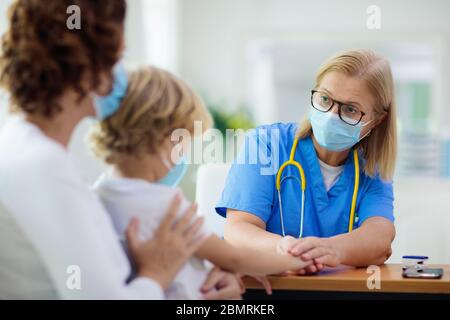 Pediatrician doctor examining sick child in face mask. Ill boy in health clinic for test and screening. Kids home treatment of virus. Coronavirus pand Stock Photo