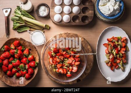 Fresh strawberries and rhubarb on wooden table background with ingredients for tasty seasonal cooking or baking. Top view. Healthy clean food. Paleo d Stock Photo