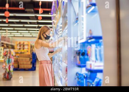 Alarmed female wears medical mask against coronavirus while purchase of household chemicals in supermarket or store- health, safety and pandemic