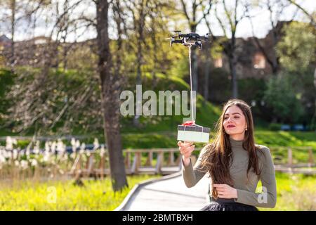 on a sunny and windy day young smiling emotional brunette receives a surprise gift delivered by quadcopter, drone delivery service, concept of modern Stock Photo