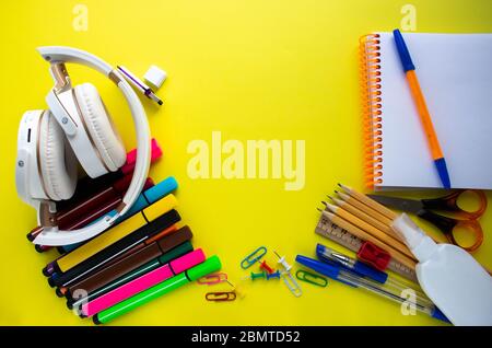 Lots of different office supplies and white headphones on a yellow background. Close-up, copy space, flat lying, top view. Stock Photo