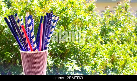 Several multicolored paper cocktail tubes in paper cup with green trees background Stock Photo
