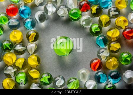 A big green glass marble  between yellow, green, blue and red marbles on a table.. Stock Photo