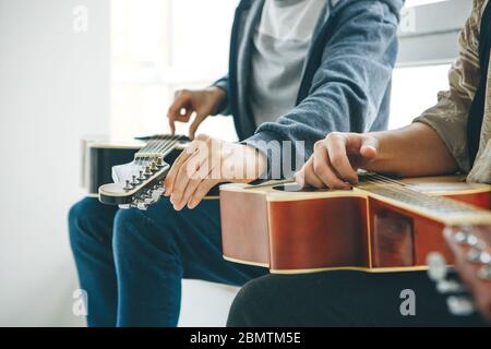 Learning to play the guitar. The teacher helps the student tune the guitar and explains the basics of playing the guitar. Individual home schooling or extracurricular lessons. Stock Photo