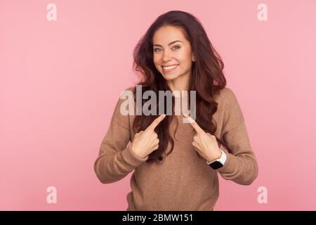 Choose me, I'm best! Portrait of optimistic boastful young woman with brunette wavy hair pointing herself and smiling to camera with contented proud e Stock Photo