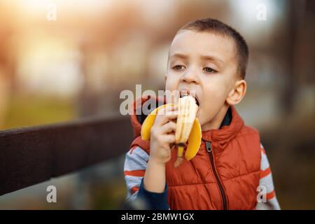 Little boy eating banana in nature.Happy kid enjoy eating fresh fruit. Healthy food,people and lifestyle concept. Stock Photo