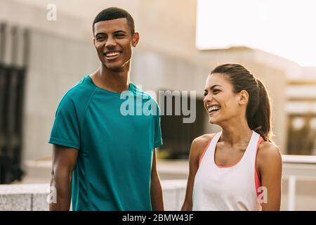 Outdoor shot of two people taking a break after running training session. Man and woman standing in the city and relaxing after a workout. Stock Photo