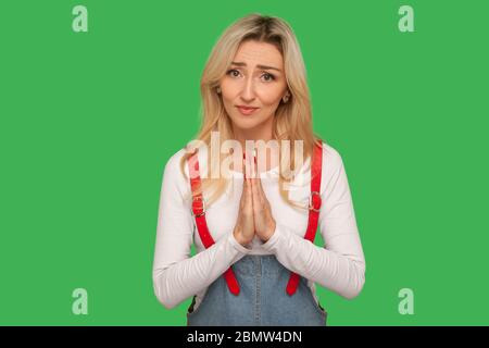 Portrait of worried pleading adult woman in denim overalls praying for help, appealing with guilty apologizing expression, sincere saying please. indo Stock Photo