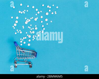 Pile of white pills medicine spilled over shopping cart on blue background. Creative pharmaceutical or medical concept for drugstore, pharmacy, online Stock Photo