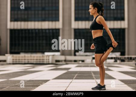 Fitness woman stretching outdoors. Sporty female doing warm up exercise in morning in the city. Stock Photo