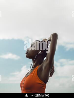 Side view of a fitness woman with arms stretching warmup exercise outdoors. Female in sportswear doing stretches outdoors against sky. Stock Photo