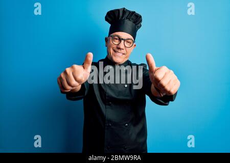 Middle age handsome grey-haired chef man wearing cooker uniform and hat approving doing positive gesture with hand, thumbs up smiling and happy for su Stock Photo