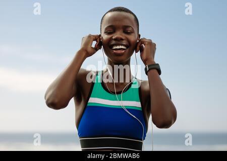 Sportswoman enjoying listening music while having break outdoors after training session. African woman runner wearing earphones to listen music after Stock Photo