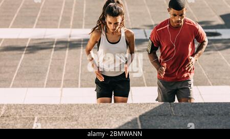 Couple in sportswear training together in the city. Sporty man and woman exercising on steps together in the city. Stock Photo