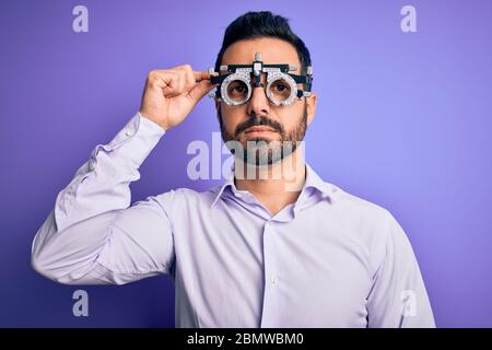 Young handsome optical man with beard wearing optometry glasses over purple background with a confident expression on smart face thinking serious Stock Photo