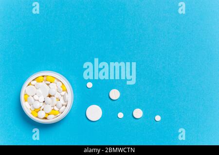 Medicine bottle with white pills and yellow capsules inside and dosis of different size pills outside on blue background. Madication and prescription Stock Photo