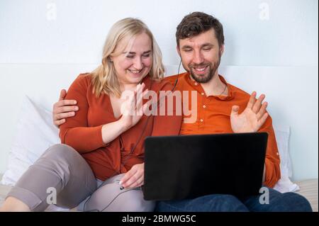 Smiling young adult couple using laptop and waving their hands Stock Photo