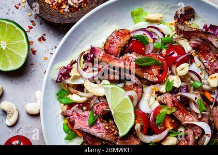Asian beef salad with vegetables and nuts in a white bowl on a dark background. Asian food concept. Stock Photo