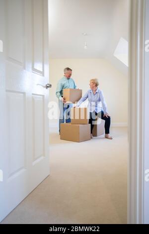 Senior Couple Downsizing In Retirement Carrying Boxes Into New Home On Moving Day