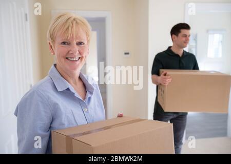Portrait Of Senior Woman Downsizing In Retirement Carrying Boxes Into New Home On Moving Day With Removal Man Helping Stock Photo