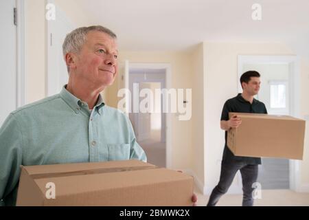 Senior Man Downsizing In Retirement Carrying Boxes Into New Home On Moving Day With Removal Man Helping Stock Photo