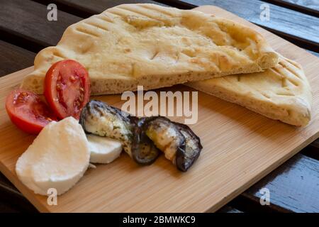 White focaccia with grilled eggplant tomatoes and mozzarella on a wooden cutting board Stock Photo